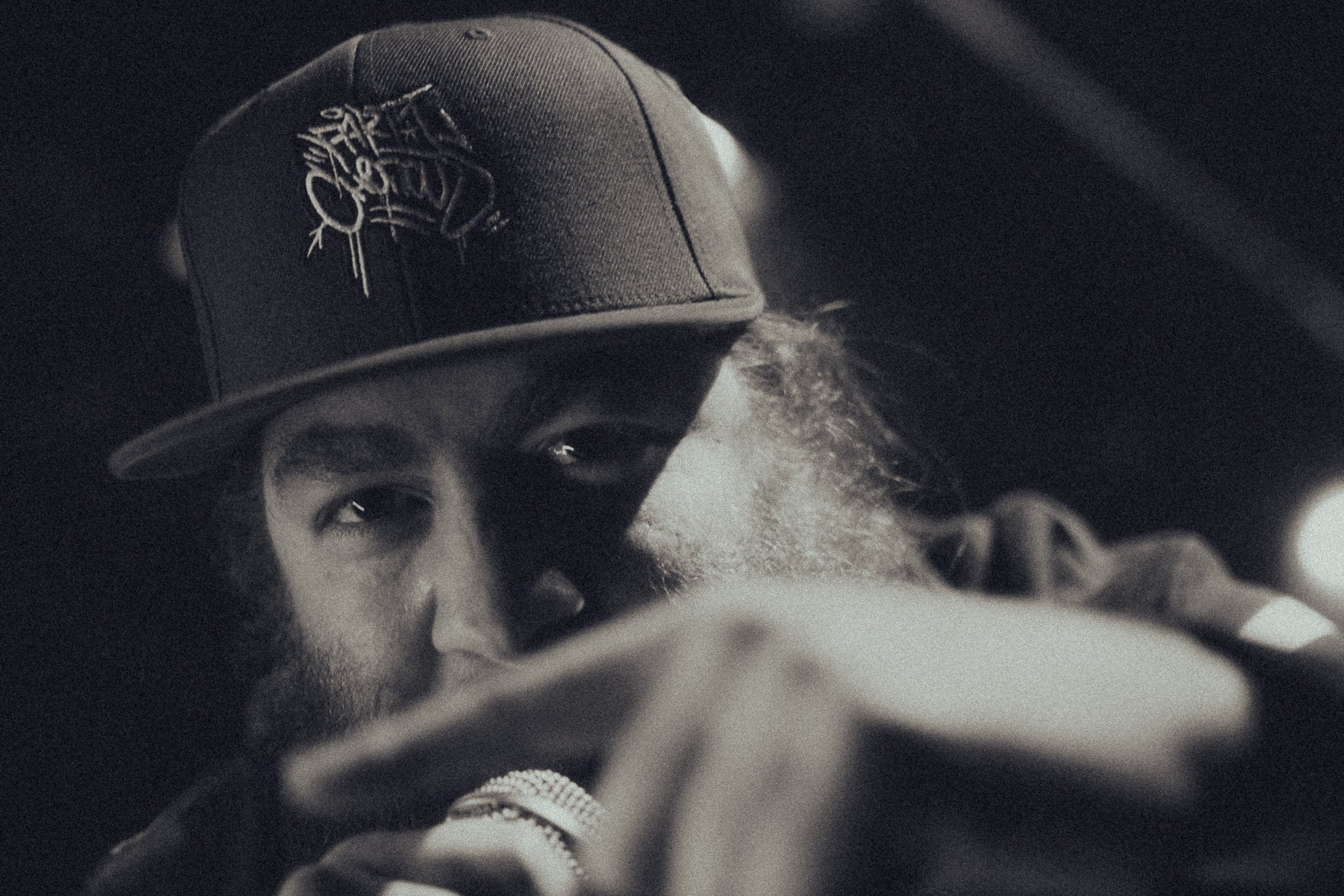 Metaphyzik wearing "Party Chenous" cap holding a microphone, in a close-up shot.